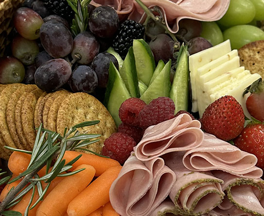 Charcuterie board with assorted cheeses, crackers, grapes, berries, and fresh rosemary garnish.